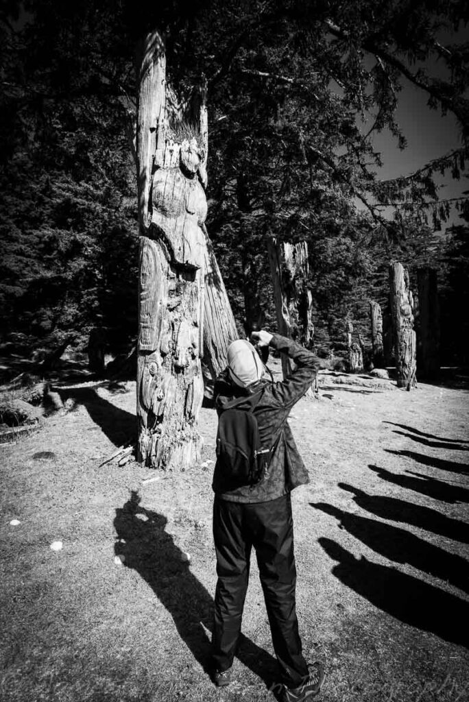 A photo tour participant at S'gang Gwaii, Haida Gwaii. These mortuary poles were erected to commemorate respected elders. The site inspires feelings of mysticism and spirituality and to me, the shadows (of the other tour participants) seemed to echo the spirits of those long gone.